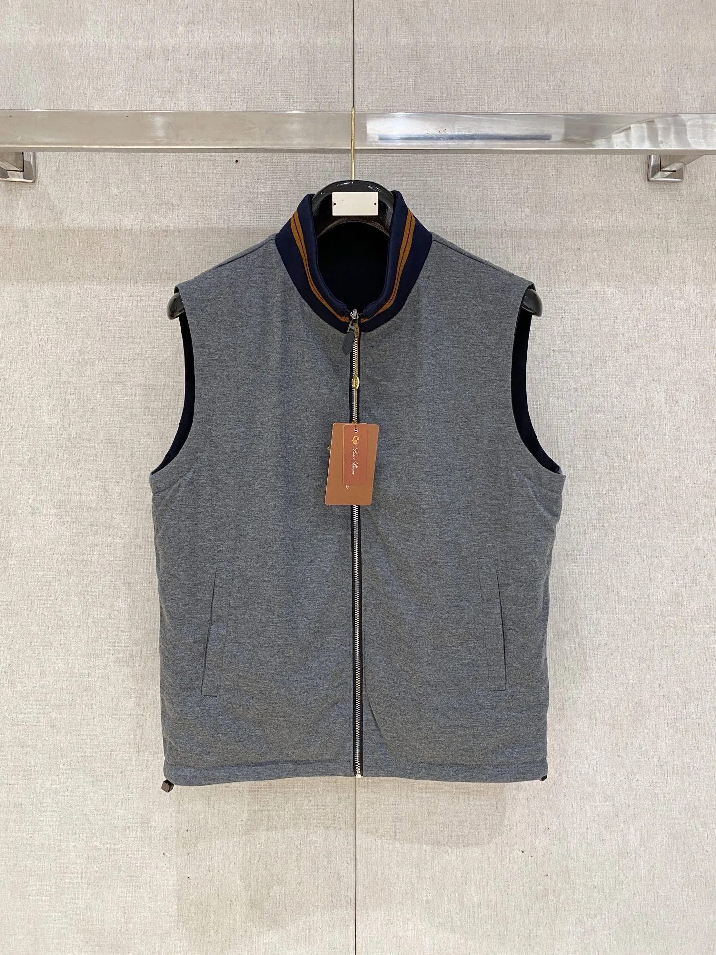 Loro Piana Reversible Stand-up Collar Vest Fabric: The front is made of high-elastic anti-wrinkle functional windproof fabric, which is smooth and waterproof, waterproof and stain-resistant, not easy to wrinkle, light and crisp; the back is made of worsted wool knitted fabric, which is soft to the touch and skin-friendly, breathable and constant temperature, one pair of fabrics, taking into account outdoor practicality and home leisure comfort, it is an old-money classic Italian commuter fabric. Design highlights: Double-wear dual-style design, the functional side is smart and business-like, and the knitted side is soft and elegant, allowing you to switch between two atmospheres when wearing one set; The brand logo is embroidered with the same color on the left chest, which is low-key and subtle, unobtrusive and highlights the texture; Brown trim strips are spliced ​​on the side of the pocket, with metal snaps, and the light luxury details are full; The collar is closed with contrasting brown and yellow striped ribs, and the hem has drawstring adjustments on both sides to tighten the fit. Version and structure: Improved high stand-up collar tailoring, fits the neck without getting stuck, and modifies the shoulder and neck lines; Slightly loose straight cut, accommodates all body shapes, can be worn with shirts, polo, and thin knitted fabrics without restraint; Symmetrical welt pockets with metal snap buckles for stable storage of items and preventing them from slipping. Style positioning: Light business commuting, Premium casual, outdoor travel wear, minimalist, low-key and noble, Versatile is a must-have item for mature men. Color: Black, Navy Blue (the reverse side is Gray knitted surface) Sizes: M-4XL